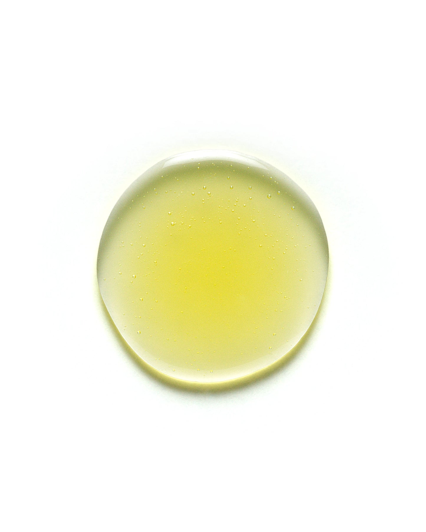 Close-up of a golden yellow droplet of Yerba Santa Micellar Cleansing Oil on a white background. The oil appears translucent with tiny suspended bubbles, showcasing its lightweight, hydrating texture. Skincare product image optimized for facial cleansing and makeup removal.